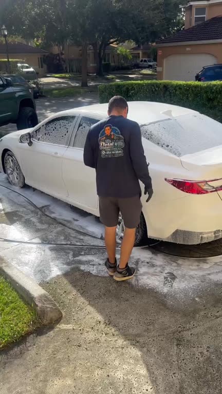 Hand washing a sedan in a driveway